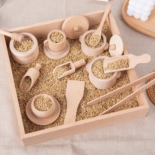 Wooden kitchen tea set toys in a tray with small bowls, cups, and utensils filled with grains.