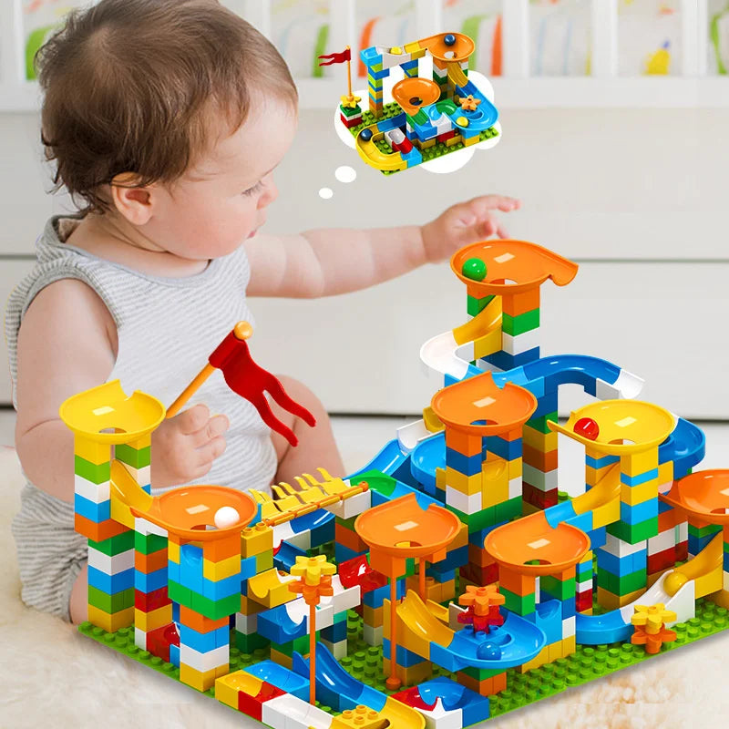Colorful building blocks arranged in a maze with funnels and slides, child playing nearby.