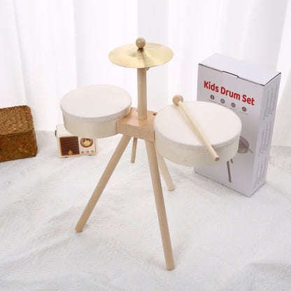 Kids drum set with two white drums, a cymbal, and wooden legs, next to a box labeled 'Kids Drum Set'.