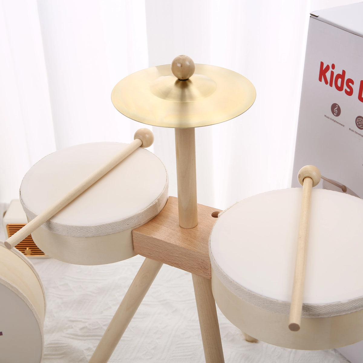 Kids drum set with two white drums, wooden sticks, and a gold cymbal on a wooden stand, bright background.