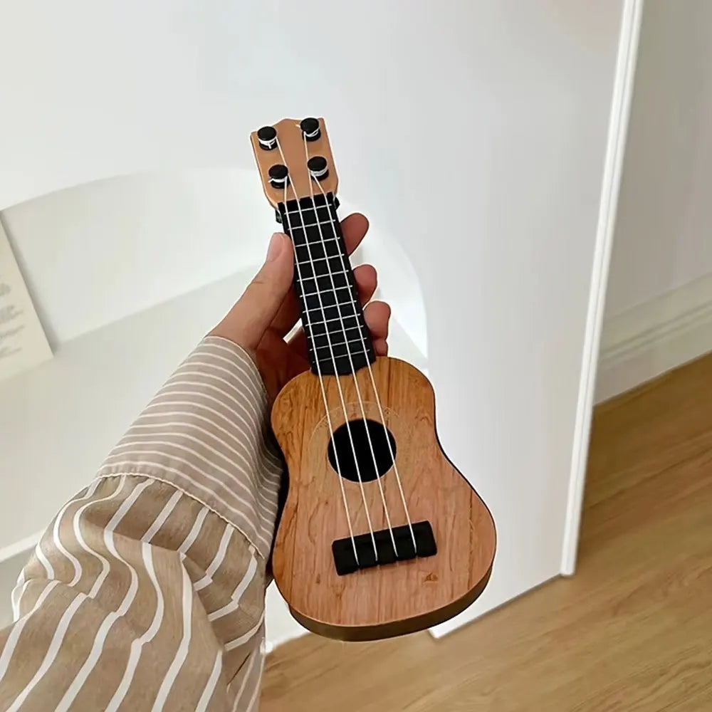 Mini classical ukulele guitar toy held in hand, featuring a wooden finish and black strings, suitable for kids.