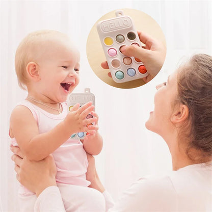 A baby holding a silicone cell phone teether toy with colorful buttons, smiling at a woman holding them.