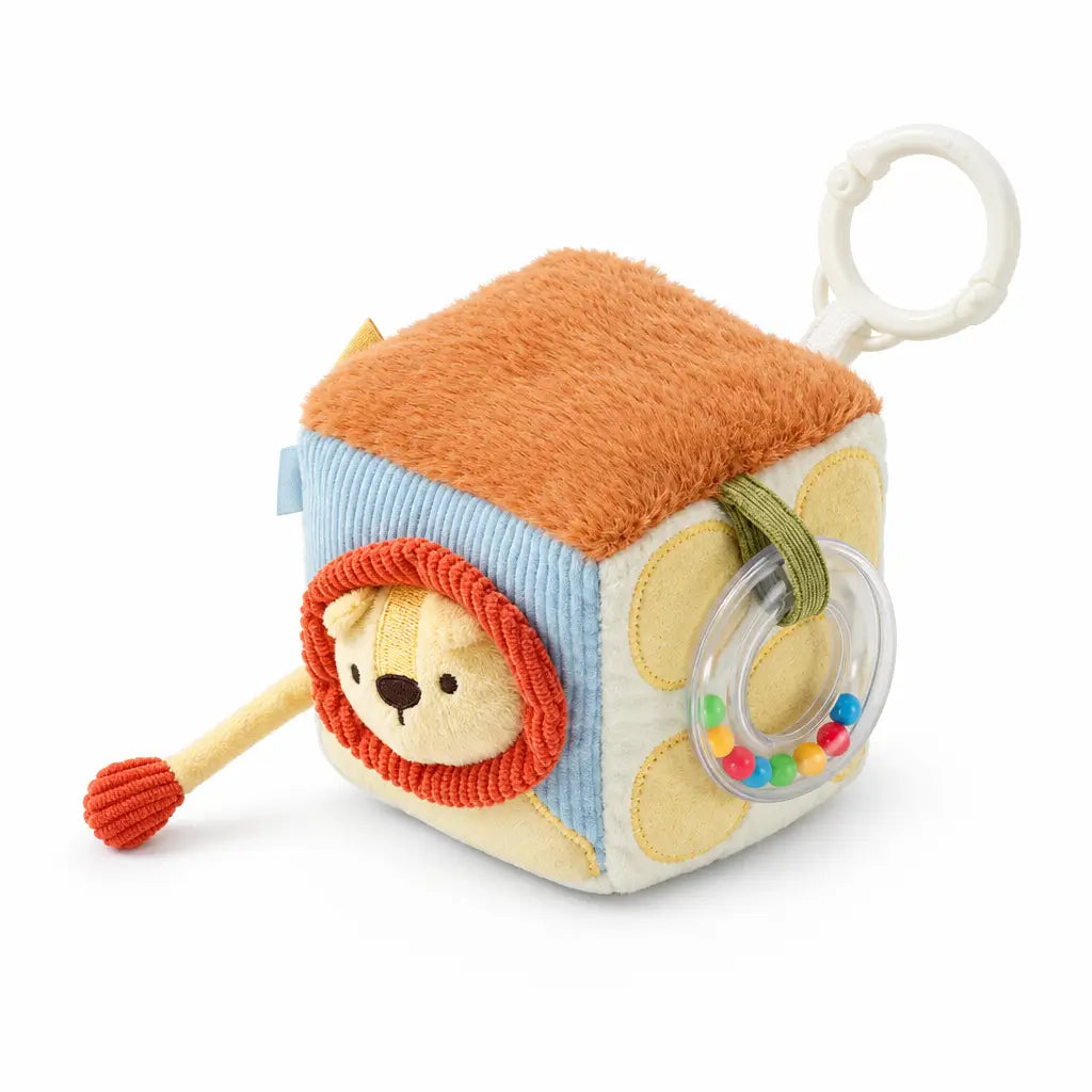 A baby sensory cube toy with a lion face, orange plush top, blue striped side, and a clear ring rattle, shown with dimension labels and a small inset instruction graphic on a white background.