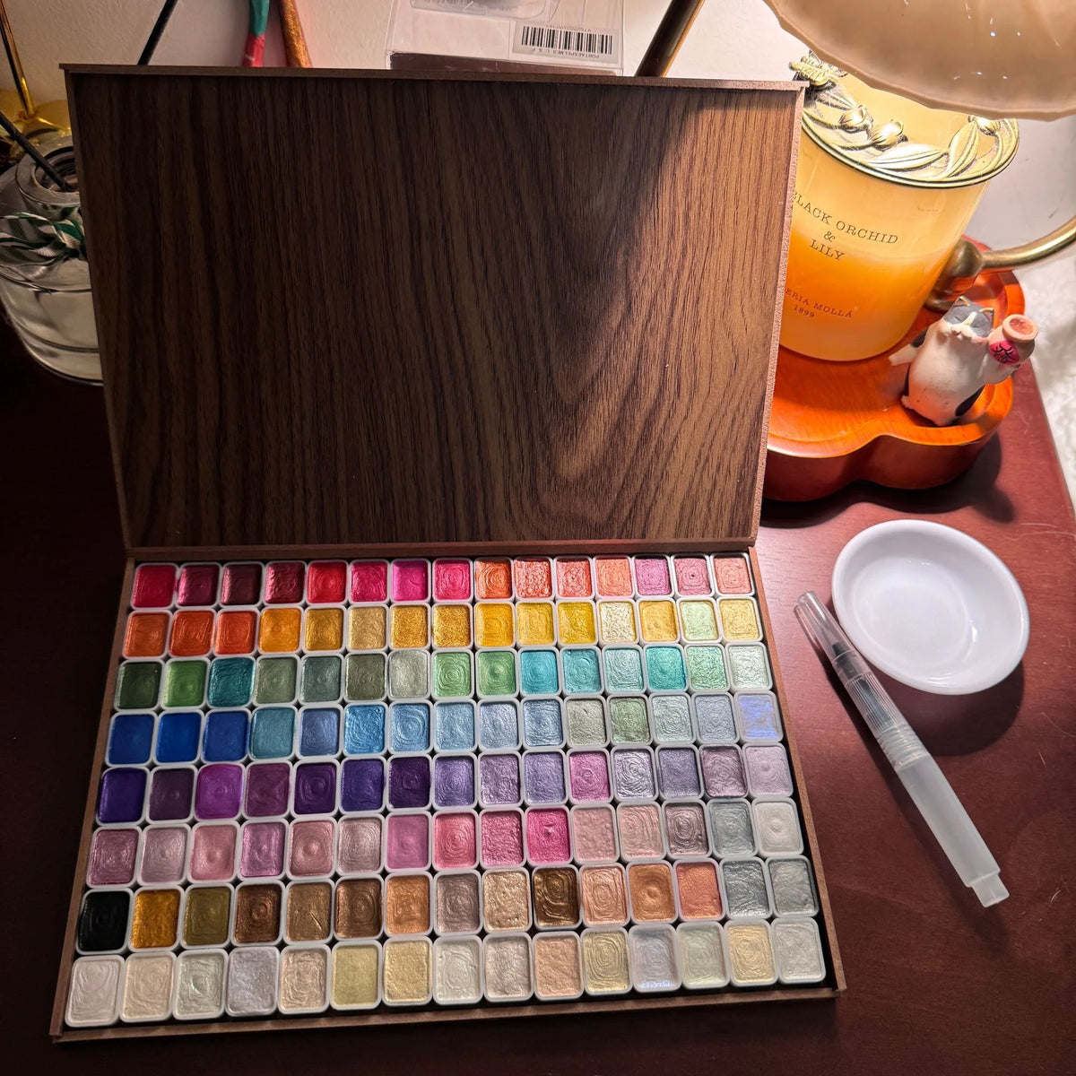 Wooden box containing 120 glitter watercolor paints in various colors, with a palette and brush beside it.