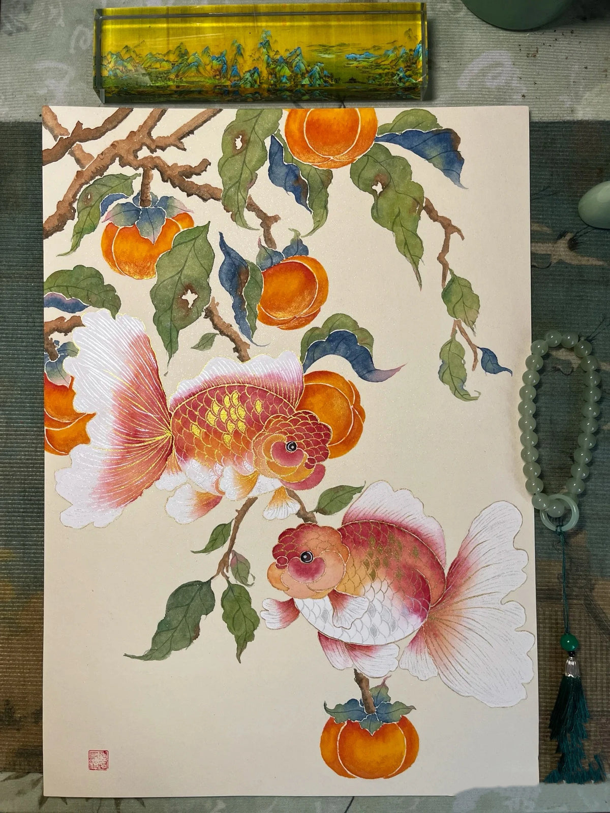 Two colorful goldfish surrounded by orange fruits and green leaves, detailed watercolor illustration on paper.