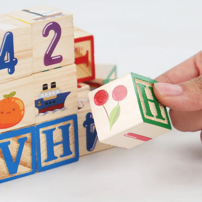 Wooden blocks featuring colorful letters, numbers, and cartoon designs, with a hand holding a block showing green letter H