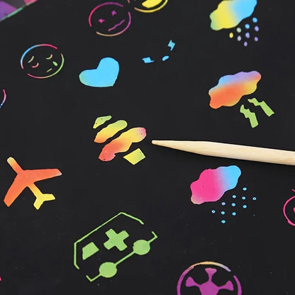 Colorful scratch paper sheets featuring various fun designs like clouds, smiles, and vehicles, with a wooden stylus.