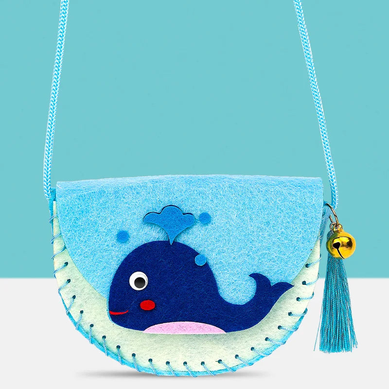 Whale-shaped crossbody purse in light blue and green felt with stitched details and a bell charm.