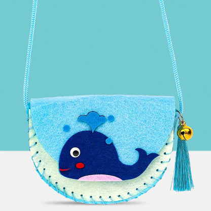 Whale-shaped crossbody purse in light blue and green felt with stitched details and a bell charm.