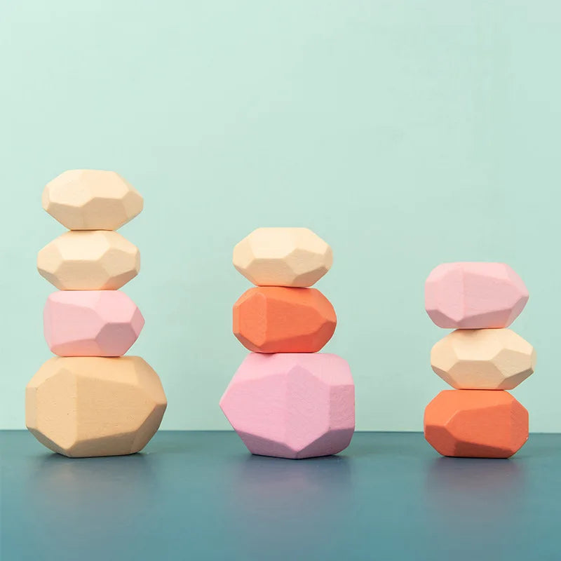 Colorful wooden stacking rocks in pink, orange, and natural wood tones, arranged in three towers on a blue surface.