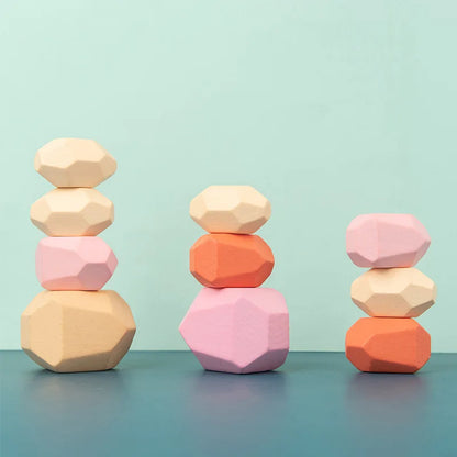 Colorful wooden stacking rocks in pink, orange, and natural wood tones, arranged in three towers on a blue surface.