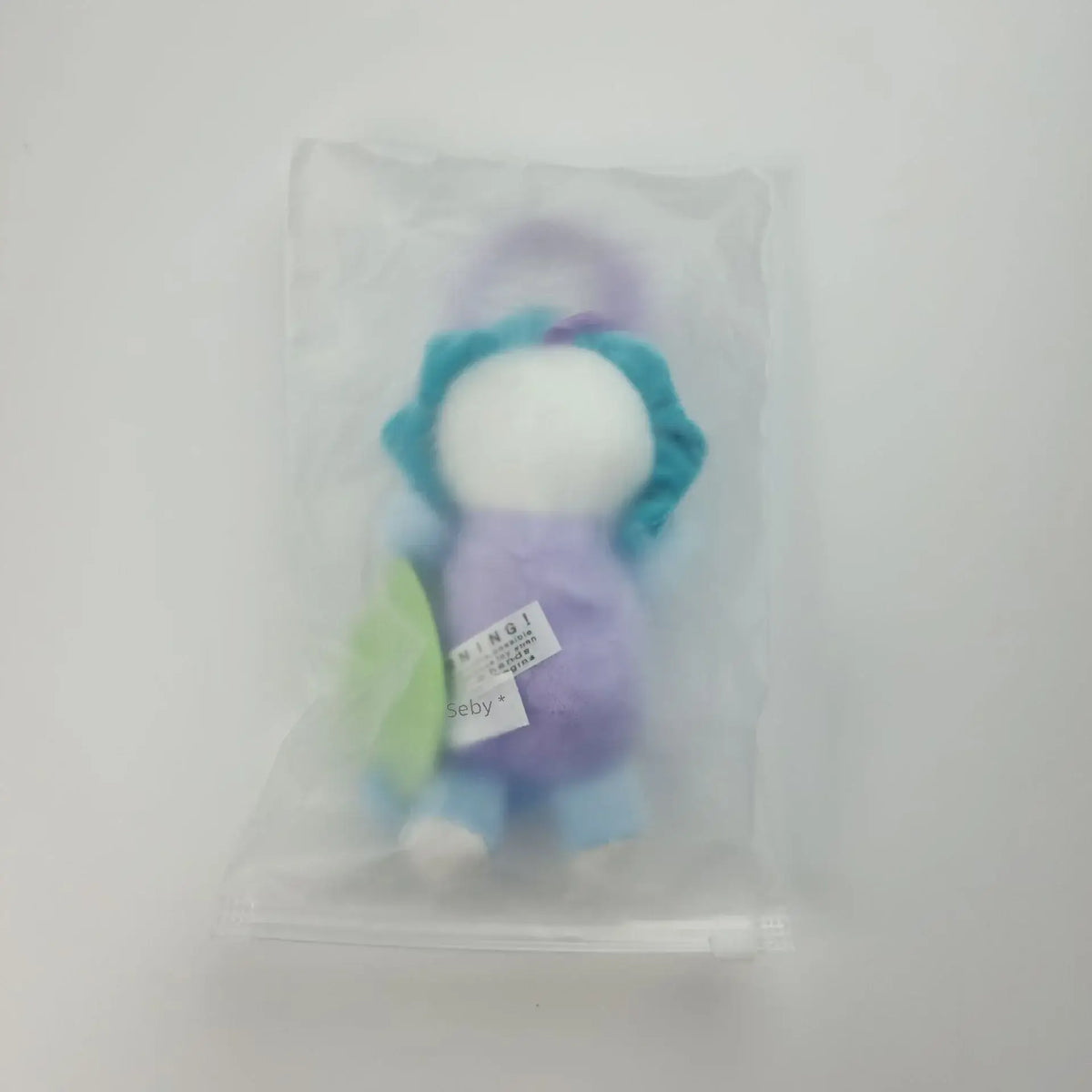 Soft stuffed animal rattle in a clear plastic packaging, featuring pastel colors and a crinkle texture.